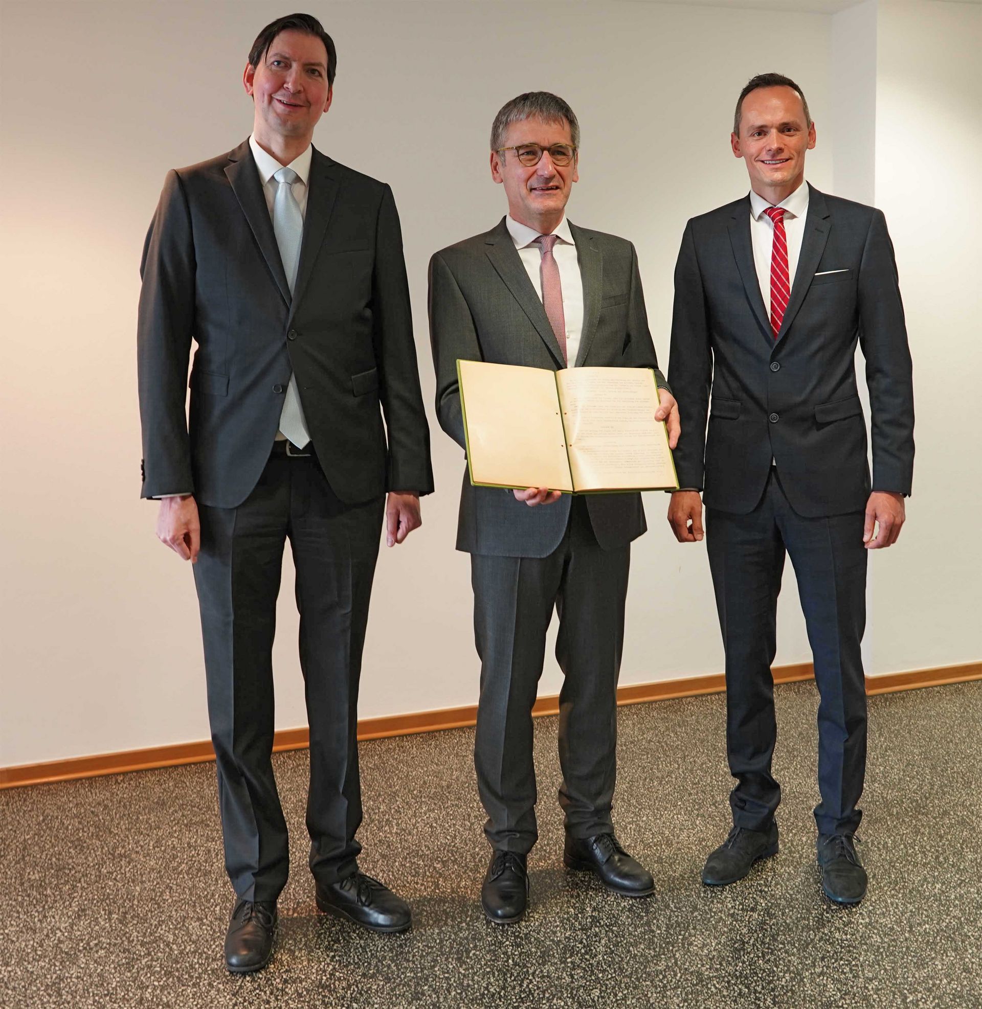 Christian Ziereis (l.), State Parliament President Hendrik Hering, and Georg Ziereis (r.) handing over the facsimile of the original of the Constitution of the State of Rhineland-Palatinate